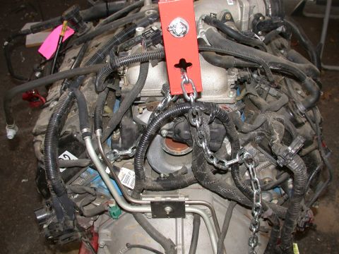 1964 Ford Ranchero - Engine assembly with numerous hoses and wiring harnesses, suspended by chains and a red lifting bracket.