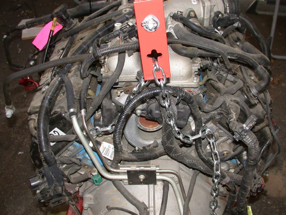 V8 engine out of the vehicle with wiring harness and red lifting plate chained to a hoist