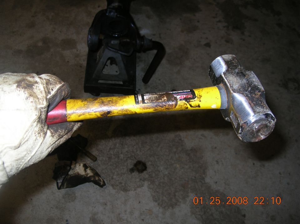 Gloved hand holding a sledgehammer with a jack stand in the background. Date stamp reads 01.25.2008