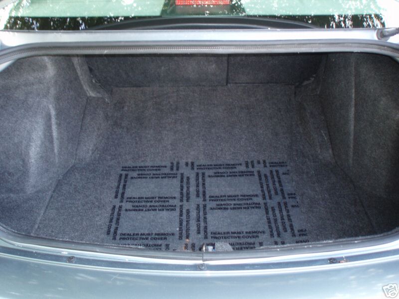 Car trunk interior with gray carpet and protective plastic mats that say "DEALER MUST REMOVE PROTECTIVE COVER"