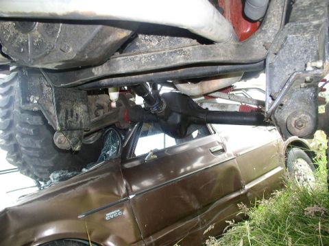 1979 Ford Bronco - The undercarriage of a large vehicle is seen above a severely damaged car with a 'CVCC' badge visible on its fender.