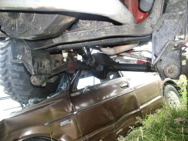 Underside of a lifted 4x4 straddling a crushed brown Honda CVCC sedan