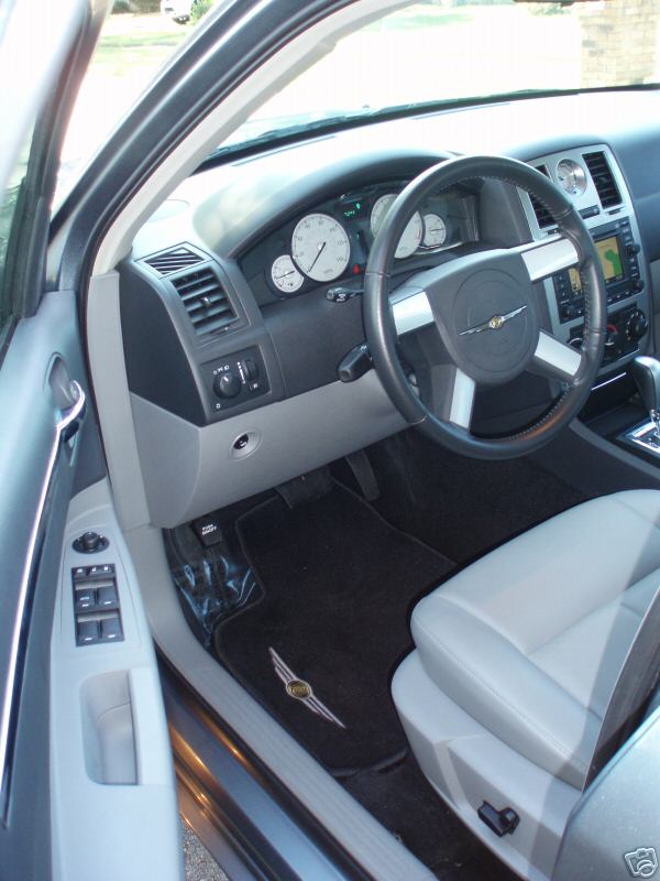 Gray leather seat and dashboard of a car with a Chrysler logo on the steering wheel and floor mat