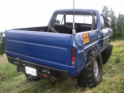 1979 Ford Bronco - A blue pickup truck modified with large off-road tires is viewed from the rear.