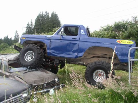 1979 Ford Bronco - A blue 1979 Ford Bronco is parked on top of another vehicle, crushing it.