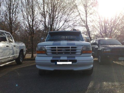 1991 Ford Crown Victoria - A white Ford F-Series truck is parked outdoors with other vehicles, under a bright sun and bare trees.