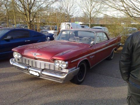 1991 Ford Crown Victoria - This red vintage coupe has a distinctive grille and chrome accents, parked outdoors.