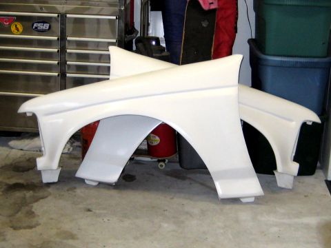 1996 Ford Bronco - Two white fiberglass or painted front fenders resting on the floor of a garage, with wheel arch openings visible. They are propped up in fr…
