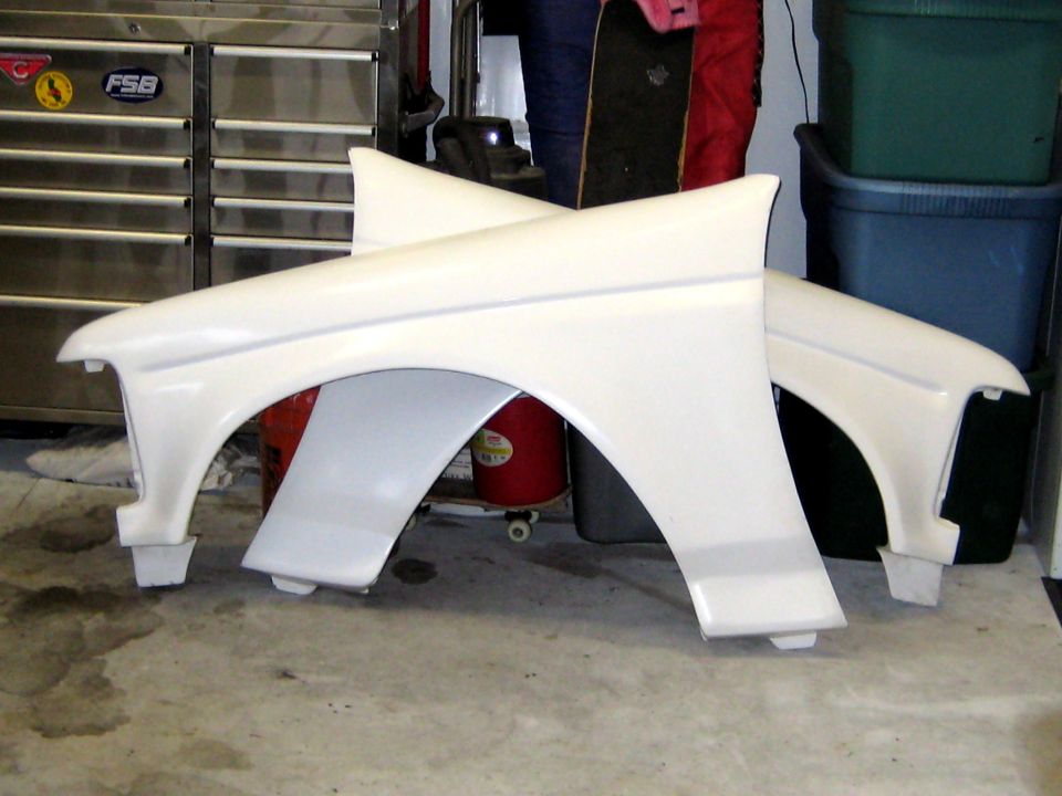 Two white front fenders resting on a garage floor near a tool chest