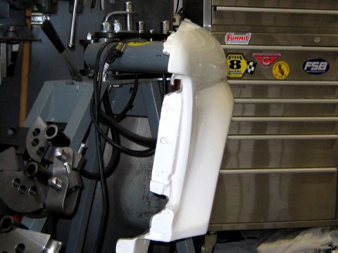 1996 Ford Bronco - A white fiberglass or plastic body panel, likely a fender or quarter panel section, clamped upright in a shop for fitting or fabrication wo…