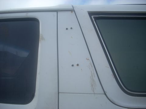 1992 Ford Bronco - Tight upper-body shot of a white SUV's rear quarter panel between the door glass and the fixed side window, showing four dark bolt heads mo…