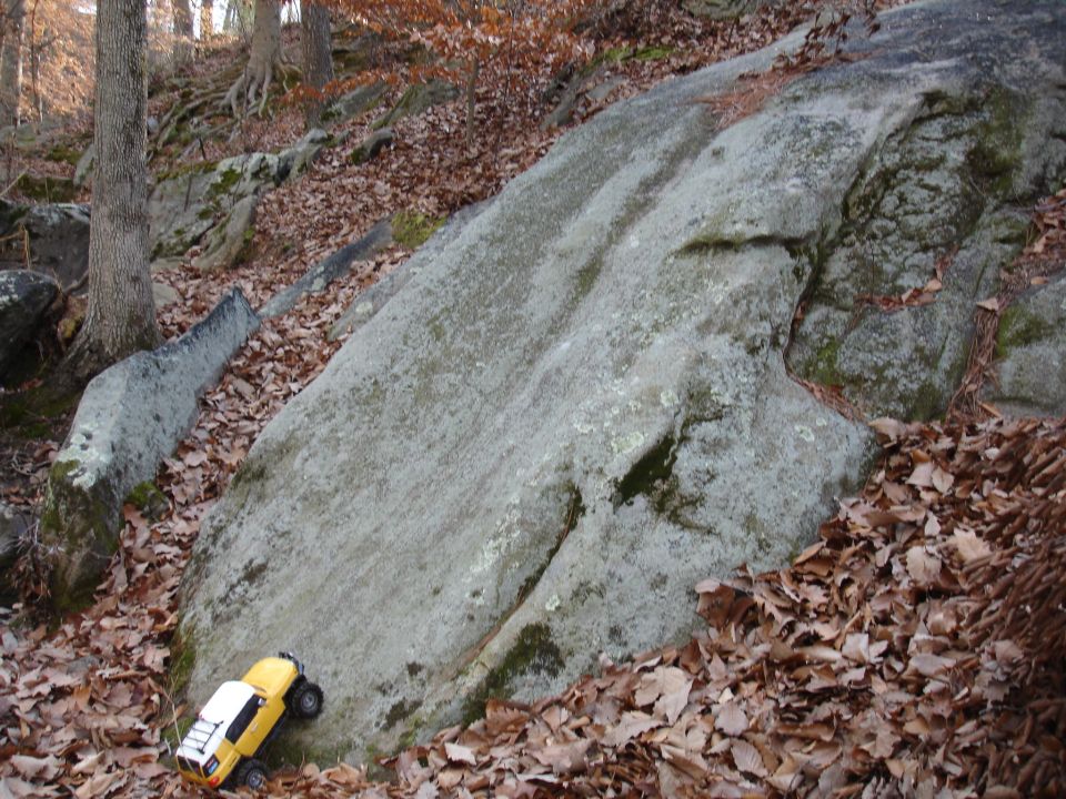 Yellow and white RC rock crawler truck parked on a large rock formation in a wooded area