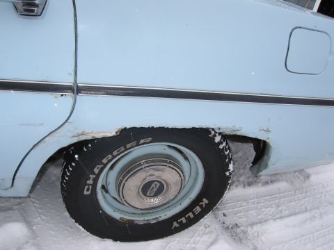 1991 Ford LTD Crown Victoria - Close-up of the rear wheel well of a light blue sedan, showing rust damage and Kelly Charger tires in the snow.