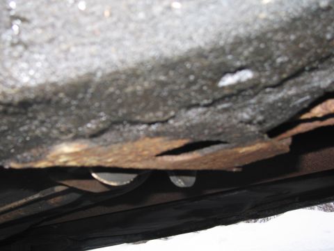 1991 Ford LTD Crown Victoria - The undercarriage of the vehicle shows significant rust and damage, with holes visible in the frame.
