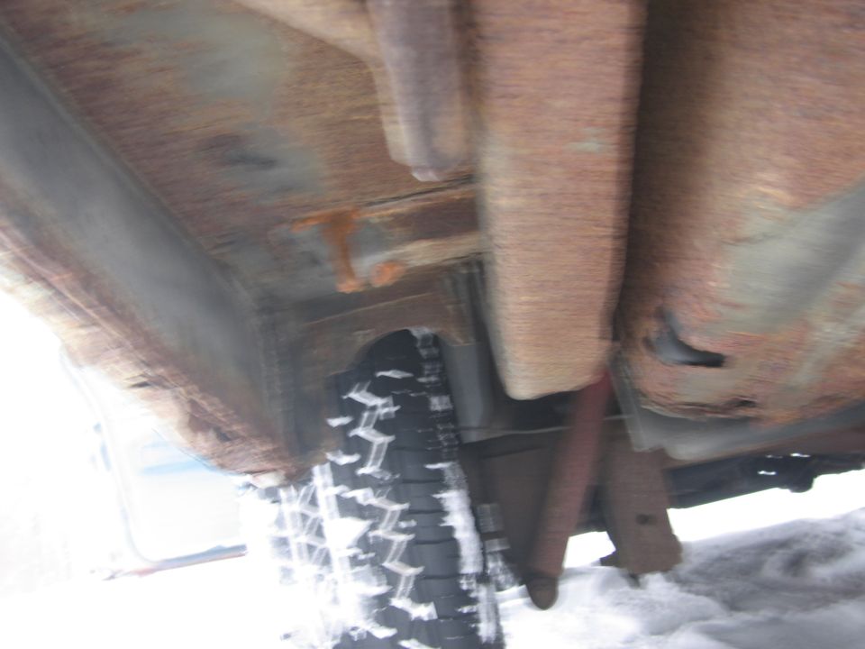 Undercarriage view showing significant rust on frame rails and body panels, with a tire and shock absorber visible