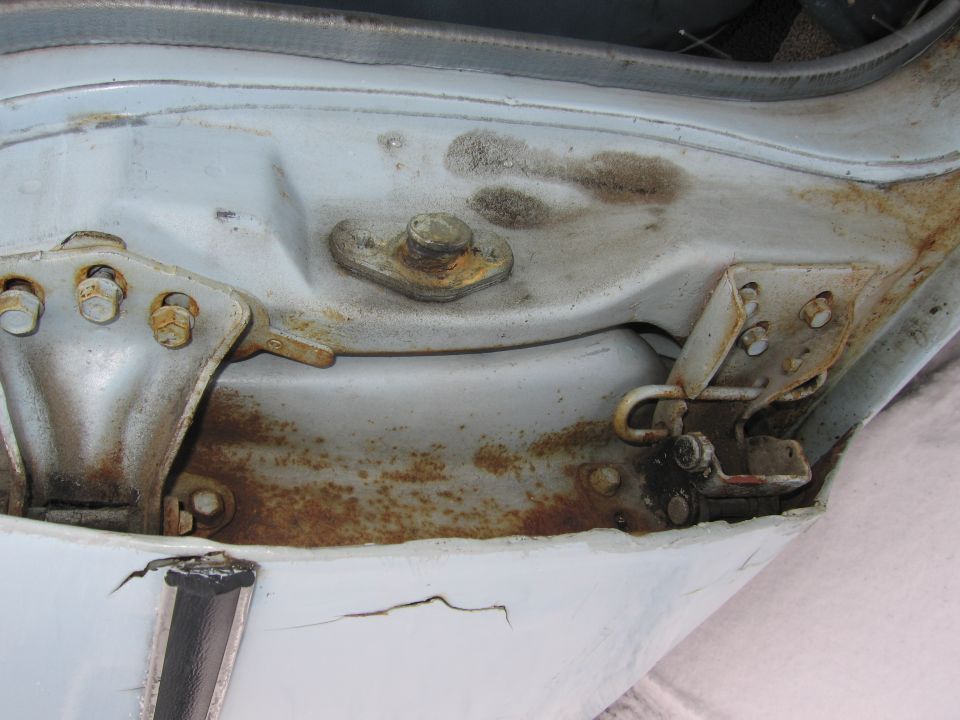 Light blue car door frame with rusted hinges and latch mechanism. Cracks visible in the paint
