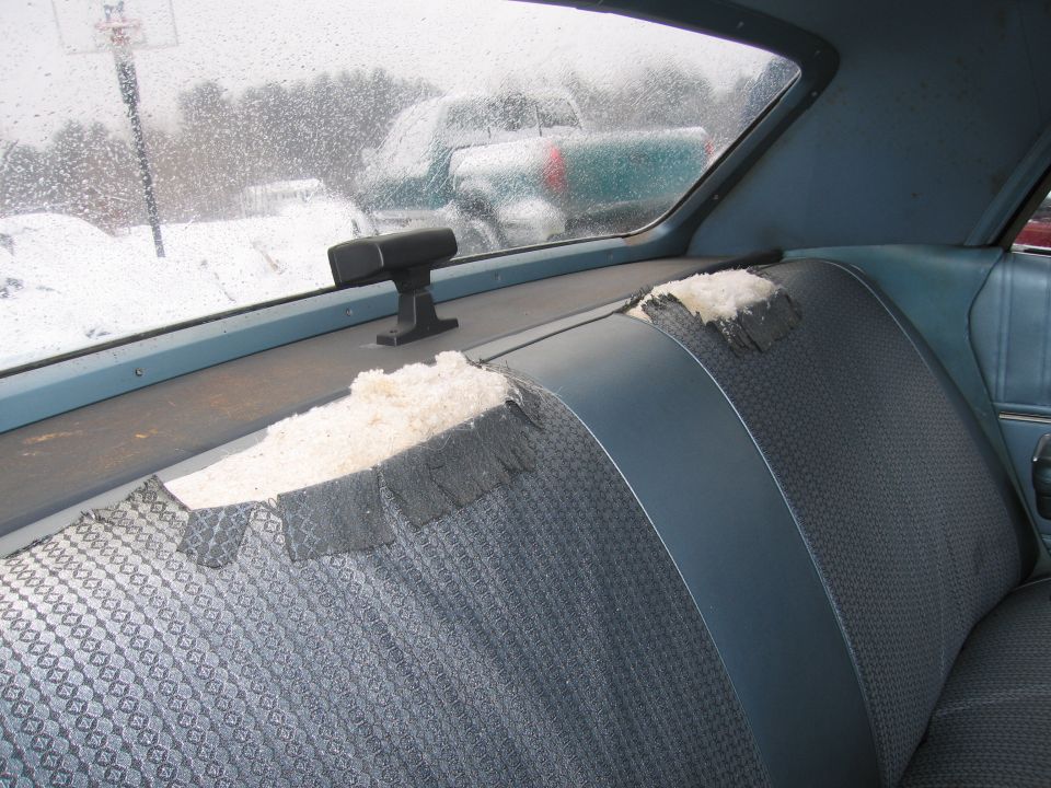 Torn rear seat upholstery and headliner in a car, with other vehicles visible through the window