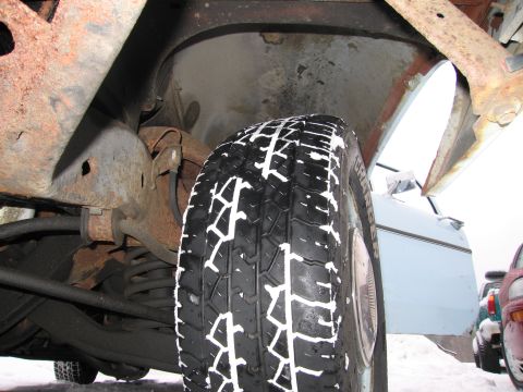 1991 Ford LTD Crown Victoria - A close-up view of a tire and the rusty undercarriage of a vehicle, with a portion of a light blue car door visible.