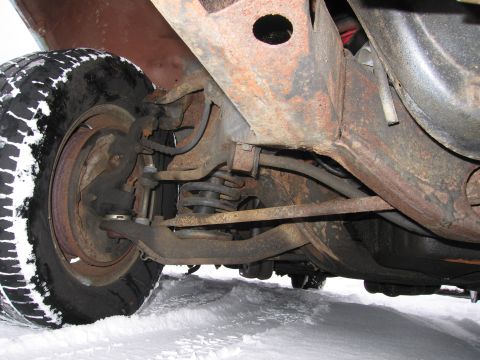 1991 Ford LTD Crown Victoria - The underside of a vehicle shows its suspension components and a snow-covered tire.
