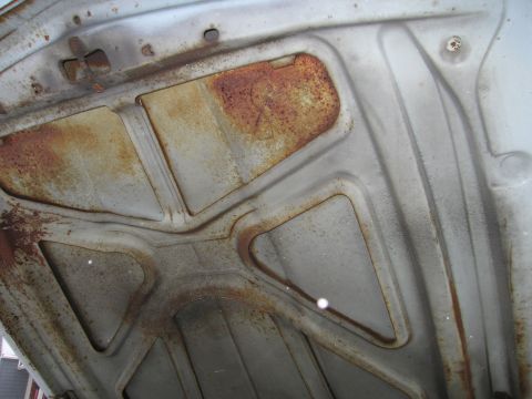 1991 Ford LTD Crown Victoria - The underside of a car hood displays significant rust and wear, obscuring any specific year or model identification.