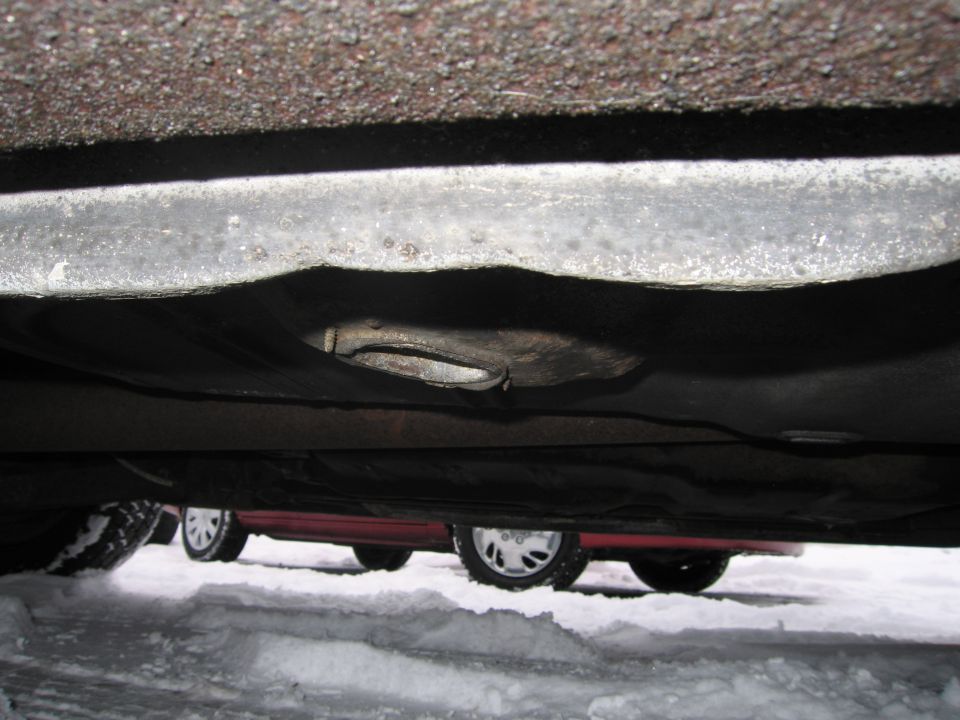 Underside view of a car, with snow on the ground and another car visible behind it