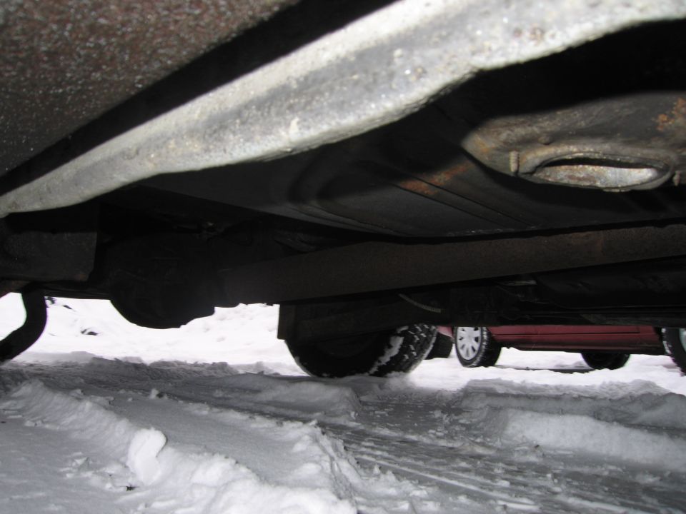 Underside view of a car in snow, with another car visible behind it