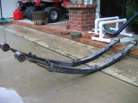 1983 Ferrari Enzo - Two leaf springs are shown resting on a concrete driveway, with an ATV visible in the background.