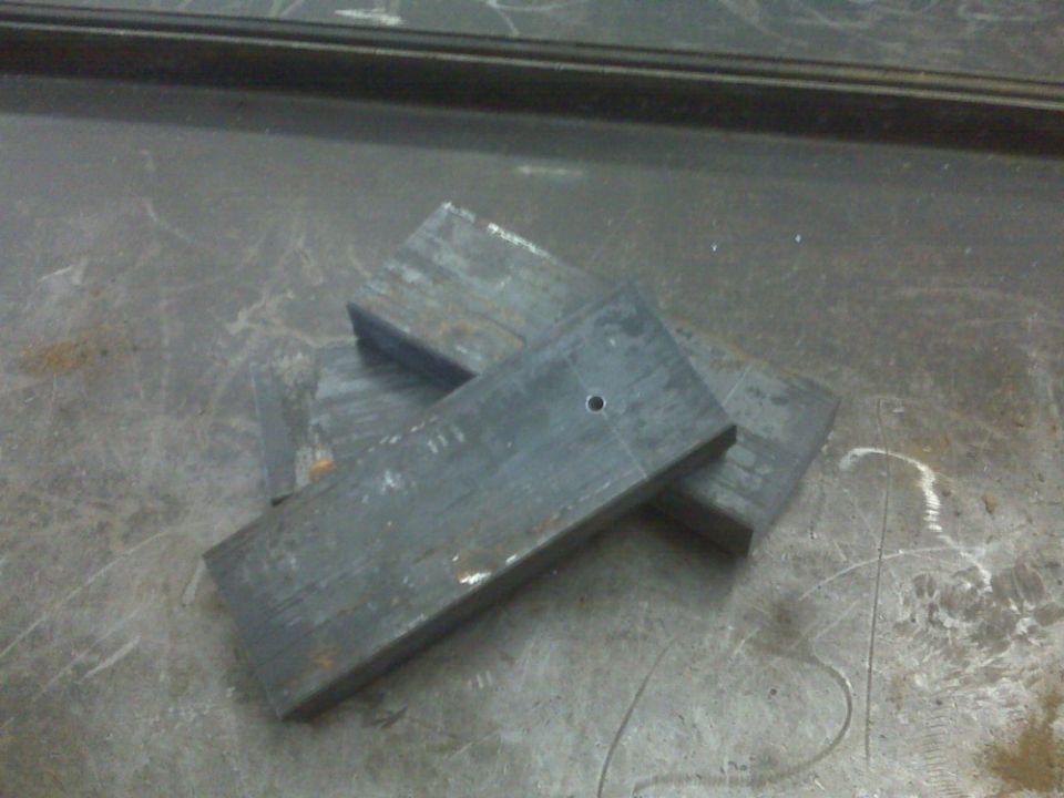 Pile of rectangular metal plates, one with a small hole drilled in it, on a scratched metal surface