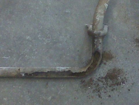 1996 Ford Bronco - A corroded metal pipe with a mounting bracket is visible against a concrete surface.