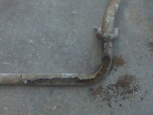 rusted metal pipe with a bracket, lying on concrete