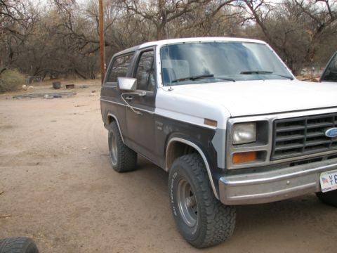 1982 Ford Bronco - This Ford Bronco is parked outside with trees and a dirt lot in the background.