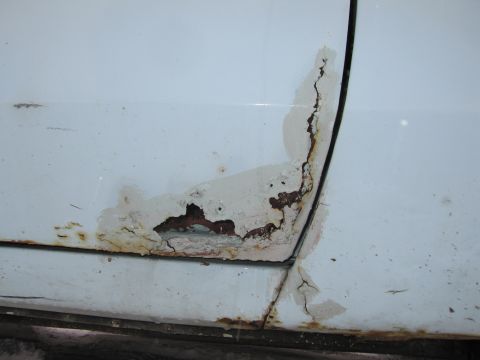 1991 Ford LTD Crown Victoria - Extensive rust and corrosion are visible on the lower section of a white car door, indicating significant wear and tear.