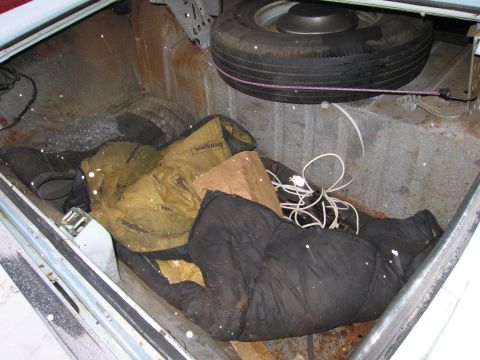 1991 Ford LTD Crown Victoria - The trunk of a vehicle contains a spare tire and various items, including sleeping bags and electrical cords.