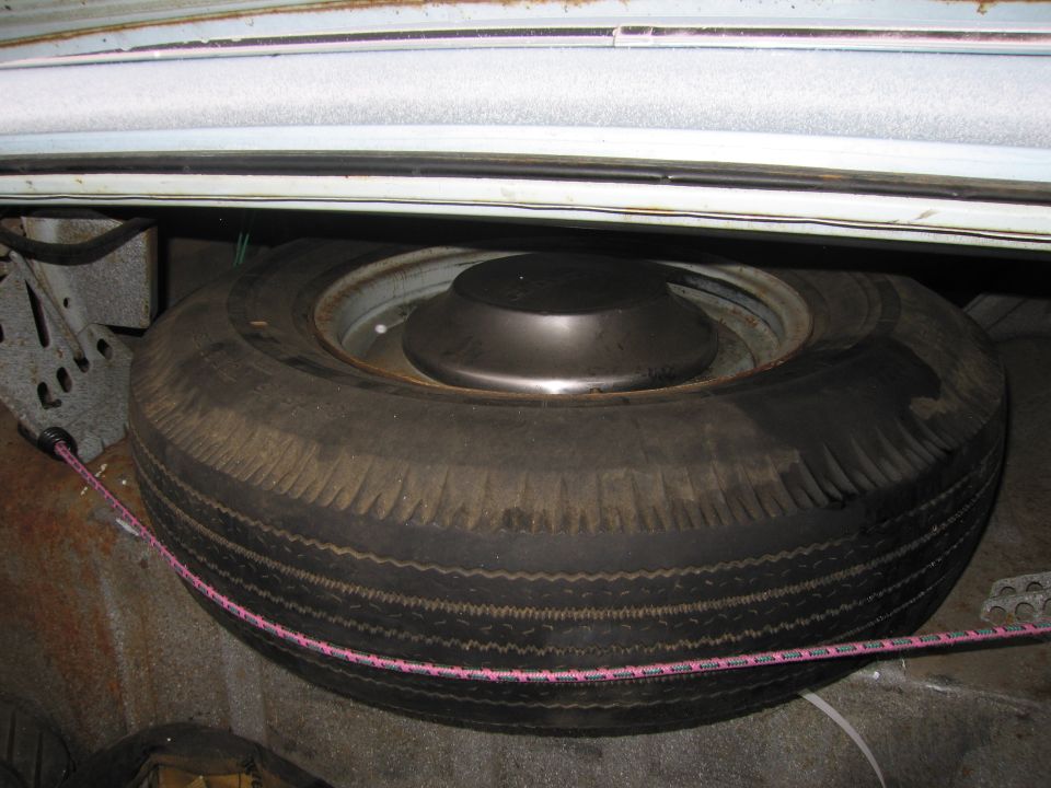 Spare tire and hubcap in a car's trunk, with visible rust on the car's body