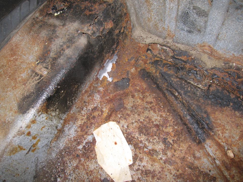 rusted metal floor pan with holes and black undercoating