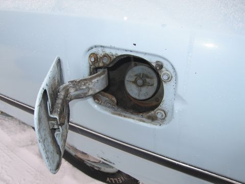 1991 Ford LTD Crown Victoria - The fuel door and cap of a white car are visible, with signs of rust and dirt around the opening.