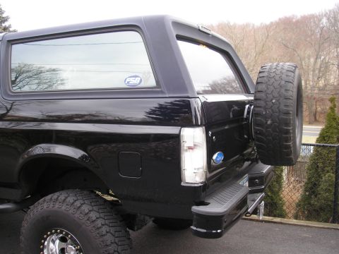1995 Ford Bronco - The rear of a black Ford Bronco is shown with a spare tire mounted on the tailgate.