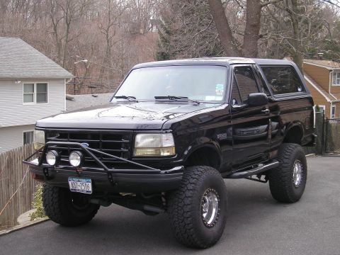 1995 Ford Bronco - A black 1995 Ford Bronco is parked in a driveway, an aftermarket bull bar and off-road tires.