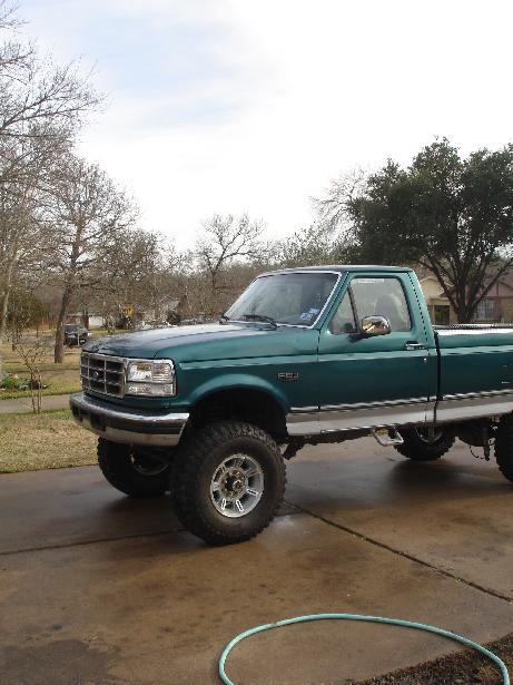 1996 Ford F-150 - A lifted green pickup truck is parked on a concrete driveway with trees in the background.