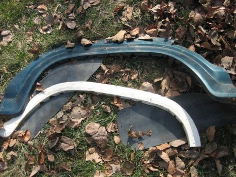 1900 Yugo Vega - Discarded car fender trim pieces are scattered on the grass amongst fallen leaves.