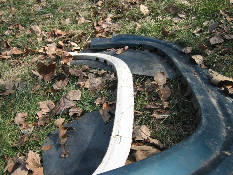 Dark green and white car fender parts on grass with fallen leaves