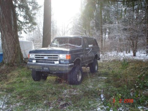 1990 Ford Bronco - A dark blue 1990 Ford Bronco with a lifted suspension sits in a snowy wooded area.