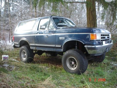 1990 Ford Bronco - This blue 1990 Ford Bronco features a lifted suspension and is parked outdoors in a snowy, wooded environment.