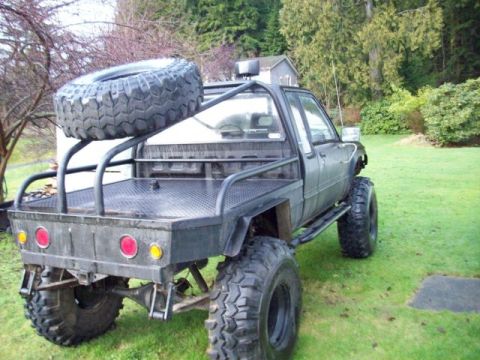 1990 Ford Bronco - A heavily modified pickup truck with a flatbed and off-road tires sits on a grassy lawn.