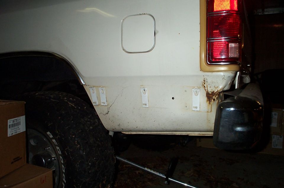 Rear quarter panel and bumper of a white SUV, showing rust and some damage