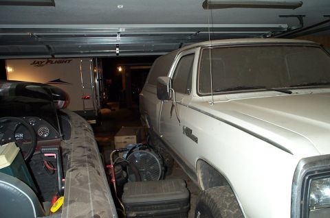 1996 Ford Bronco - A white SUV is parked inside a garage with a boat and a trailer nearby.