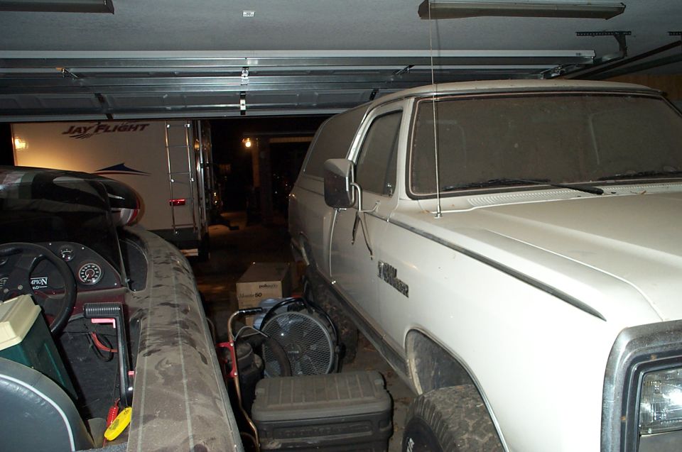 White SUV parked in a garage next to a boat and a trailer. The SUV is dusty