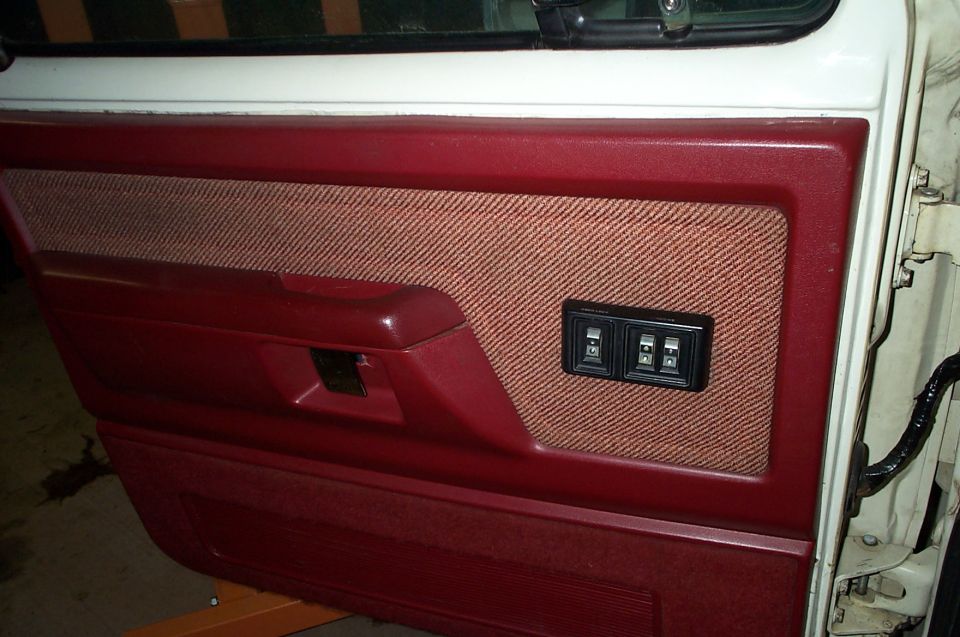 Red door panel with tan cloth insert and power window switches on a white door shell