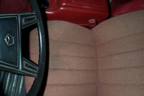 1996 Ford Bronco - Interior shot of a tan tweed cloth split-back bench seat with red vinyl trim and a red seatback release latch, alongside a black four-spoke…