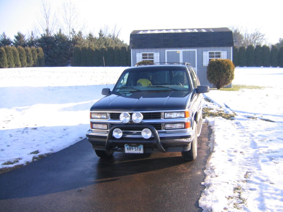 Black SUV with bull bar and auxiliary lights parked in front of a shed